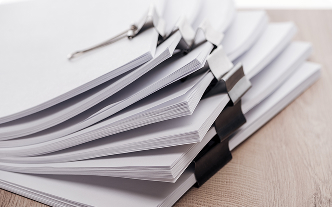 Stack of documents being held together by black clips on a wooden desk