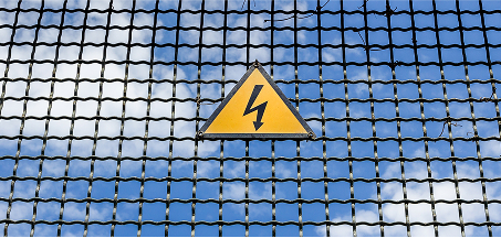A grid fence with a yellow electrical warning sign on it